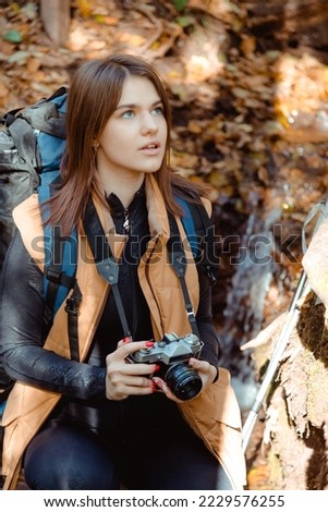 Woman traveler with camera and backpack taking photos in forest during hiking.