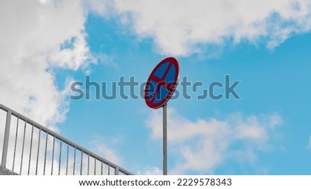 A round road sign signifying a ban on stopping vehicles against a background of blue sky and white clouds. Tools regulating the rules of the road.