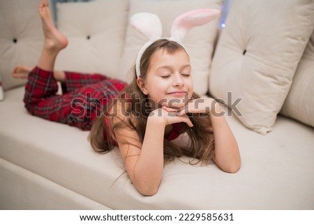 a girl with long dark hair in hare ears and red pajamas lies on the sofa with her eyes closed and dreams of christmas. High quality photo