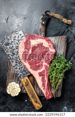 Dry aged Tomahawk rib eye steak, raw beef meat on butcher table. Black background. Top view.