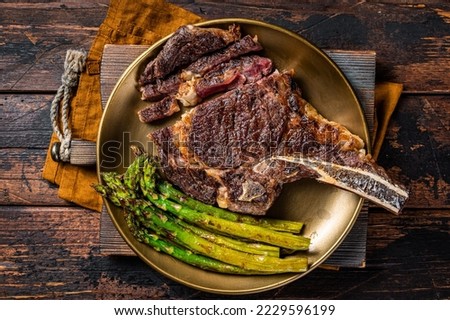 Sliced Grilled Cowboy or rib eye with bone beef steak, roasted asparagus in a plate. Wooden background. Top view.
