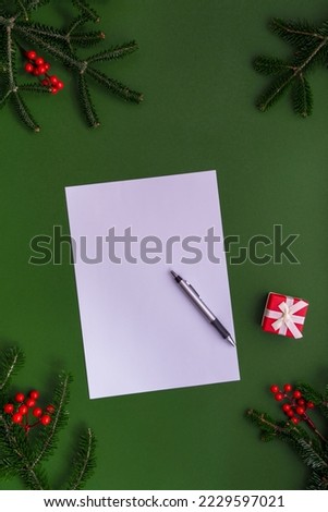 Christmas border with fir branches and presents on a green background with a white paper and pen, space for text.  Greeting card.
