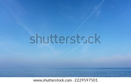 Jet plane contrails over clear blue sky and sea.