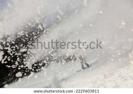 An active snowboarder freeriding on a backcountry terrain leaving a wave of powder snow behind, outdoor adrenaline adventure