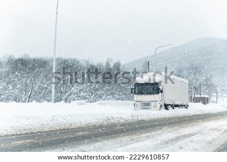 Big commercial semi-trailer truck trapped in snow drift on closed highway road at heavy snow storm blizzard cold winter day. Cargo vehicle stuck on freeway at bad weather conditions frosty snowfall Royalty-Free Stock Photo #2229610857