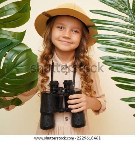 Unique child. Child blogger traveler. Kid in a safari costume. Little cute girl among palm leaves with binoculars. Child discoverer explorer traveler. Looking for treasure  Royalty-Free Stock Photo #2229618461