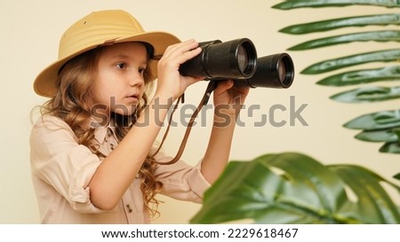 Unique child. Child blogger traveler. Kid in a safari costume. Little cute girl among palm leaves with binoculars. Child discoverer explorer traveler. Looking for treasure  Royalty-Free Stock Photo #2229618467