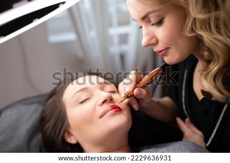 Young woman making lips tatouage in a dressing makeup room. Lips tatouage process .Woman making lips blushing. Make-up artist in beauty studio doing makeup for beautiful girl. Making mua. Royalty-Free Stock Photo #2229636931
