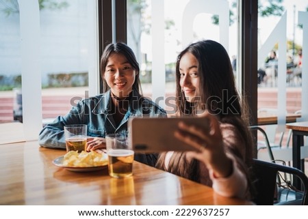 Two young women taking a selfie with the smart phone while sitting in a bar