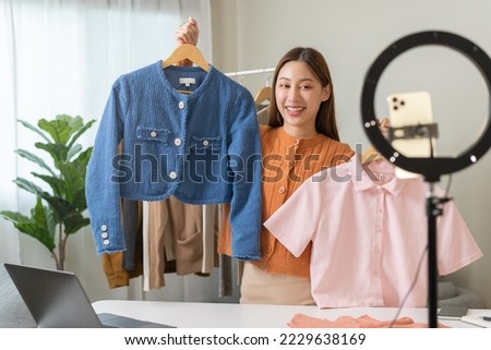 vlogger, blogger small SME business asian beautiful woman using mobile phone video call for sell clothes live stream selling online, show product present detail at home office, entrepreneur ecommerce Royalty-Free Stock Photo #2229638169