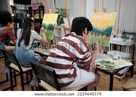 A group of student kids concentrates on acrylic color picture painting with a paintbrush on canvas in art classroom, creatively learning with talents and skills at elementary school studio education. 