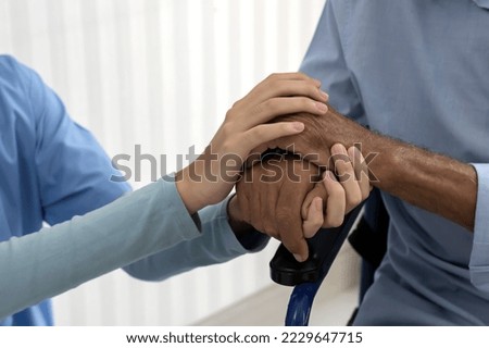 Close up care taker hands holding disabled senior hands to encourage in nursing home care