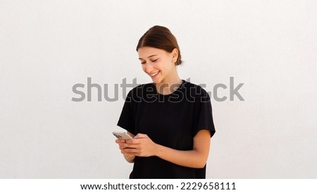 Portrait of happy young woman reading or texting message over white background. Caucasian woman wearing black T-shirt using mobile phone. Mobile communication concept