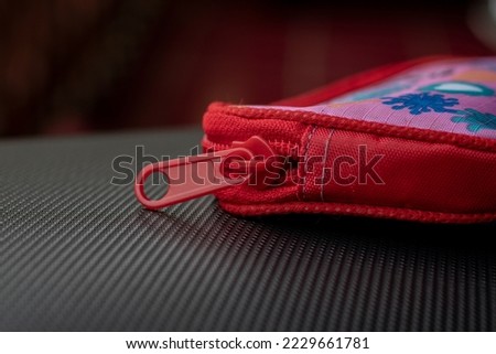 Red zipper on the wallet which is taken close up made of iron and rough textile fabric on the side of the wallet.
