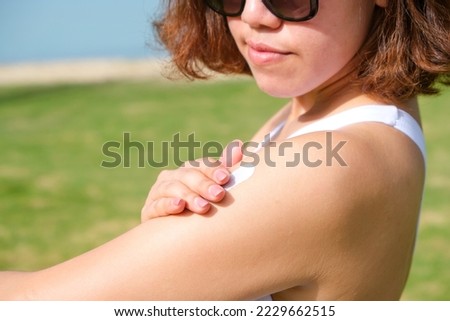 A woman is applying sunscreen and skin care to protect her skin from UV rays. She was applying sunscreen to her shoulders and arms. sunny background Health and skin care concept Royalty-Free Stock Photo #2229662515