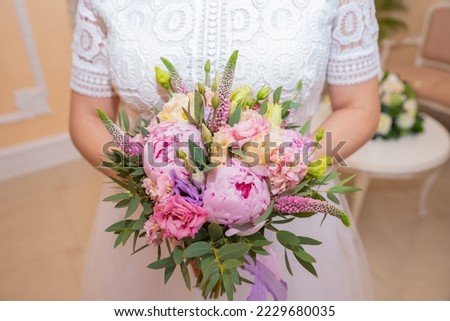 Bridal bouquet Beautiful of pink wedding flowers in hands of the bride. Close-up interior studio shot against bright background. Bouquet with peonies, eustoma and eremurus Royalty-Free Stock Photo #2229680035