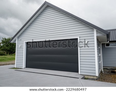 Double gray garage with black tilt-up retractable raised panel metal door and gable metal roof
