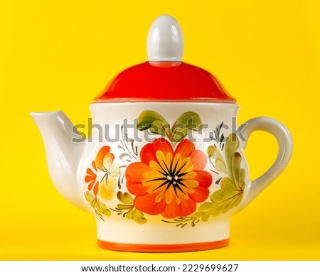 Porcelain teapot with floral ornament on a yellow background. Ceramic kettle close-up.