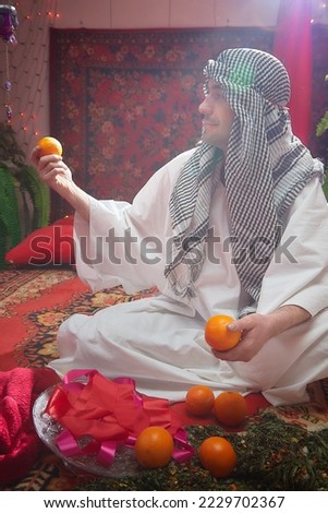 Arab sheikh in a white robe and a headscarf in a boudoir in a room with a red carpet. Oriental eastern fabulous style photo shoot with a man. Male model posing in fary tale