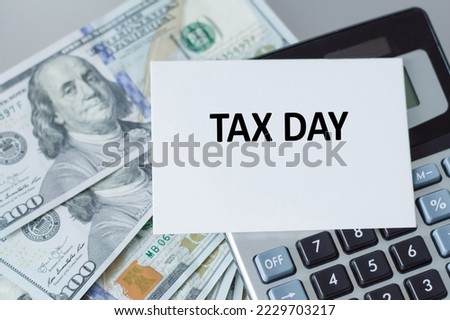 Tax Day typography text on paper card with alarm clock and calculator on wooden background