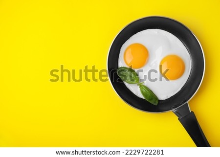 Tasty fried eggs with basil in pan on yellow background, top view. Space for text