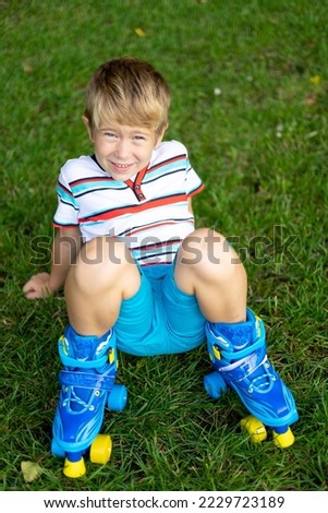 a cute little boy in roller skates is sitting on the grass, smiling, looking at the camera, the concept of sports, outdoor games, active games