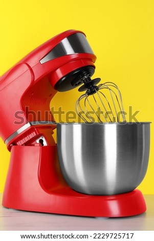 Modern red stand mixer on white wooden table against yellow background
