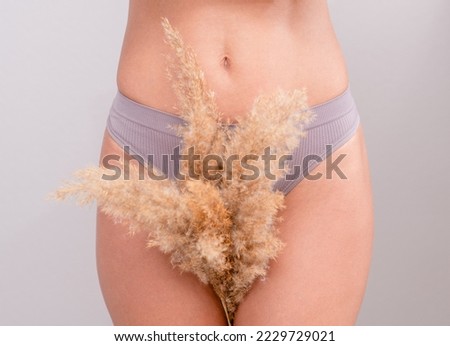 Beautiful young woman wearing gray underwear holds dry grass between legs. Hair removal of unwanted vegetation concept or refusal of depilation of the bikini zone