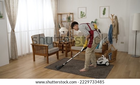 full length of an asian househusband groaning in pain for he pulled his back muscles while cleaning the house with a vacuum cleaner in the living room at home. Royalty-Free Stock Photo #2229733485