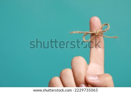 Man showing index finger with tied bow as reminder on turquoise background, closeup. Space for text Royalty-Free Stock Photo #2229735063
