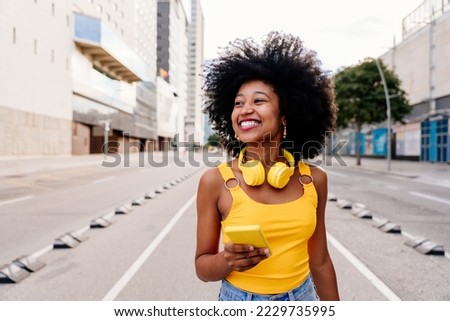 Beautiful young happy african woman with afro curly hairstyle strolling in the city - Cheerful black student walking on the streets Royalty-Free Stock Photo #2229735995