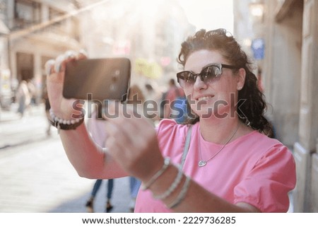 brunette woman talking on the smartphone and taking a photo with a phone in her hands. Summer sunny day in the city.
