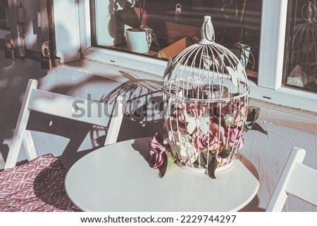 Beautiful white cage with butterflies and blooming roses., at a white table. Still life picture. 