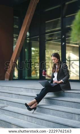 Business woman using laptop outside sitting near office building do remote work. Self employed freelance worker. Data analysis. Typing information.
