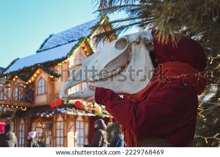 Lady holding horse skull scenic photography. Picture of woman with wintertime trade fair on background. High quality wallpaper. Photo concept for ads, travel blog, magazine, article