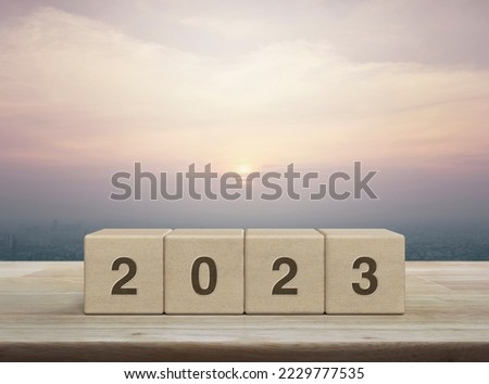 2023 letter on wood block cubes on wooden table over city tower and skyscraper at sunset, vintage style, Happy new year 2023 cover concept