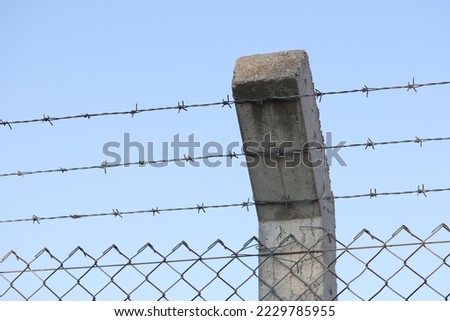 Close-up of security barbedwire fence, wire with clusters of short, sharp spikes on concrete pillar. Fence or warfare obstruction, correctional institution concept Royalty-Free Stock Photo #2229785955