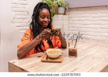 a beautiful african american woman sitting in a bar taking a picture of acai bowl with peanut butter