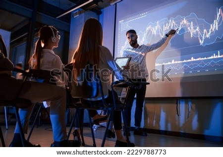 Trading teaching. Male leader talking to employees, showing the plan on the projector in office of stock exchange company.
