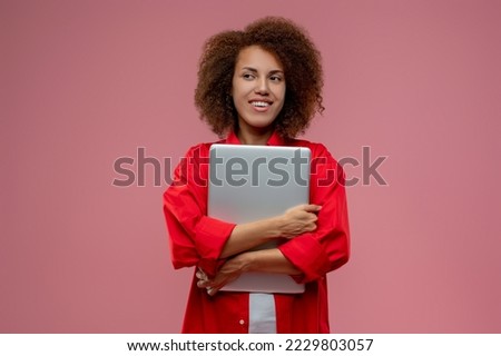 Curly-haired young woman in red jacket with laptop in hands