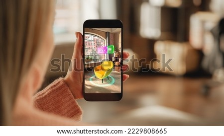 Over the Shoulder Footage of a Female Hand, Holding Smartphone with an Augmented Reality Display Showing a Chair. Woman Doing Online Shopping and Checking her Options In Live Situation In Distance Royalty-Free Stock Photo #2229808665
