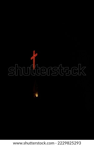 A vertical shot of a neon red cross at night