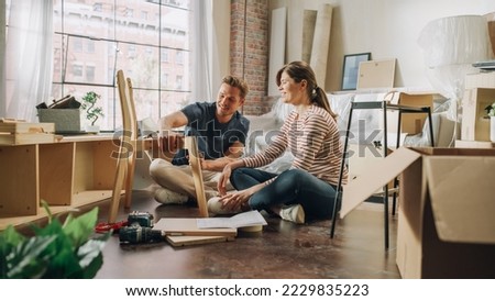 Family Moving in and Home Renovations: Happy Couple Assembles Furniture Together, Girlfriend Reads Instructions and Boyfriend Follows them with some Force. New Apartment for Young Partners in Love Royalty-Free Stock Photo #2229835223
