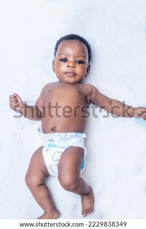 A cute four month old african baby girl wearing a white diaper cover lie down on white background.