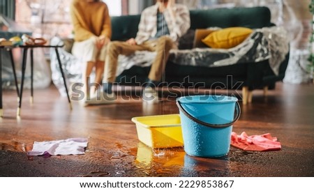 Roof is Leaking, Pipe Rupture at Home: Water Drips into Buckets in Living Room. Angry Couple in Background Calling Insurance Company, Screaming into Phone in Frustration, Trying to Find Plumber Royalty-Free Stock Photo #2229853867