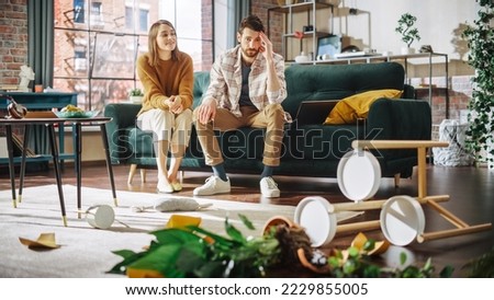 Funny Moment: Ruined Potted Flower by Dog After Overturning it and Making Mess in the Whole Apartment. Couple Sitting on Couch with look of Disbelief, Frustration. Woman Smiling Royalty-Free Stock Photo #2229855005