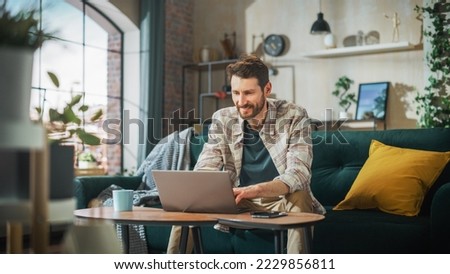 Portrait of Smiling Middle Aged Man Working from Home on a Laptop Computer in Sunny Cozy Apartment. Successful Male Entrepreneur Does Remote for e-Business Project, Online Shopping Royalty-Free Stock Photo #2229856811