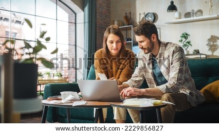 Stressful Accounting at Home: Couple Using Laptop Computer, Sitting on Sofa in Apartment. Young Family Filling Tax Forms, Mortgage Documents, Bills, Checks, Balances, Invoices are in Order Royalty-Free Stock Photo #2229856827