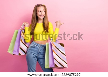 Photo of shiny impressed schoolgirl wear yellow crop top holding shoppers pointing thumb empty space isolated pink color background