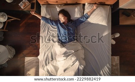 Top View Apartment: Beautiful Young Woman Sleeps Charmingly in Her Bed, Turns off Smartphone Alarm Clock, Greets a New Day with Happiness and Smiles. Top Down Royalty-Free Stock Photo #2229882419